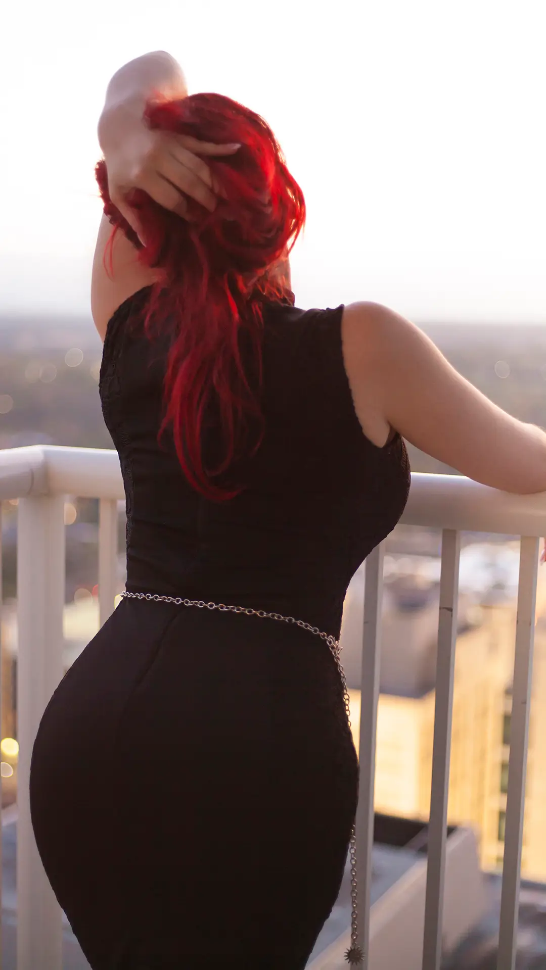Mel Mariposa from behind in a little black dress holding up her hair