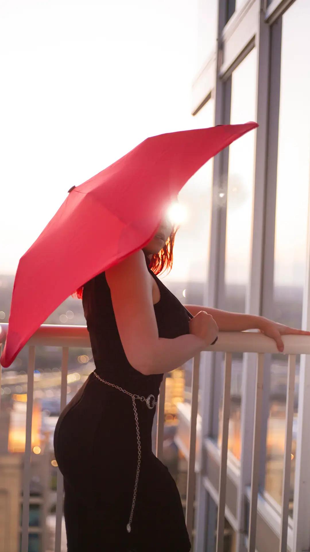 Mel Mariposa in profile wearing a little black dress and peeking out from under a red umbrella